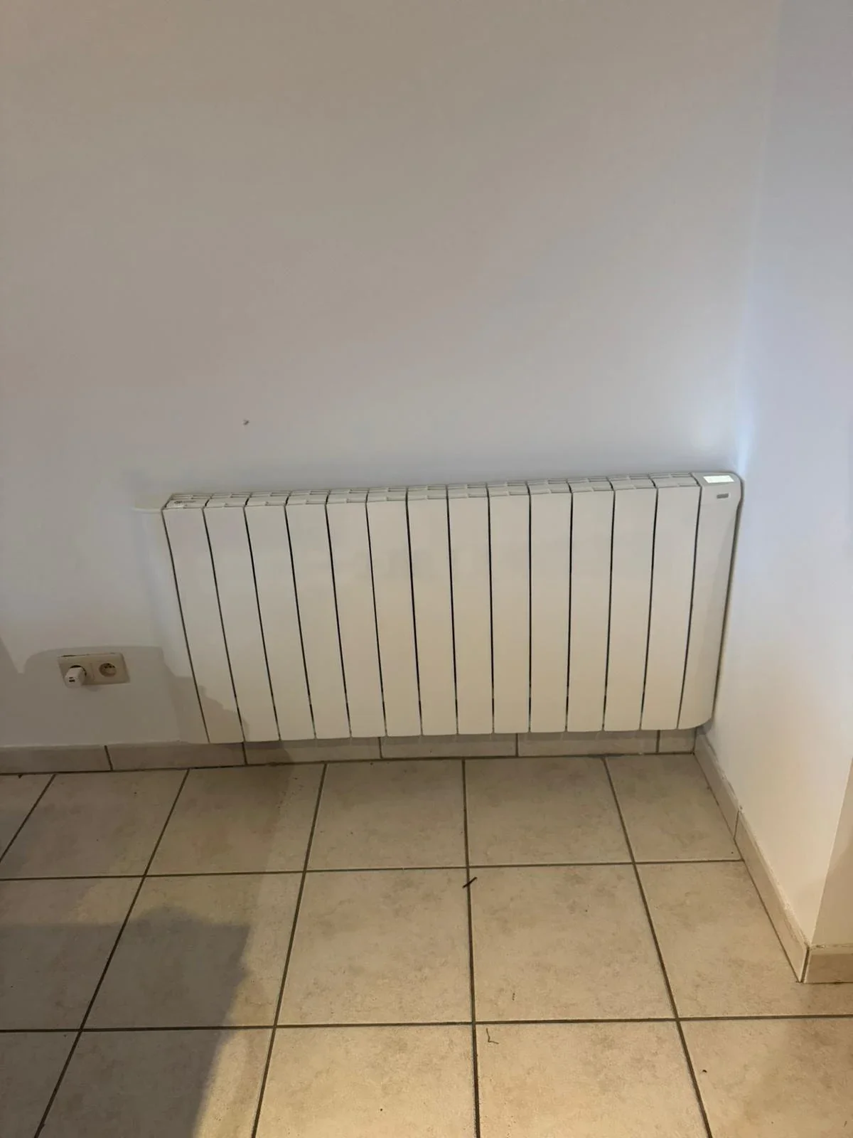 Radiateur Eco Chaleur installé sur mur clair au-dessus d'un sol carrelé